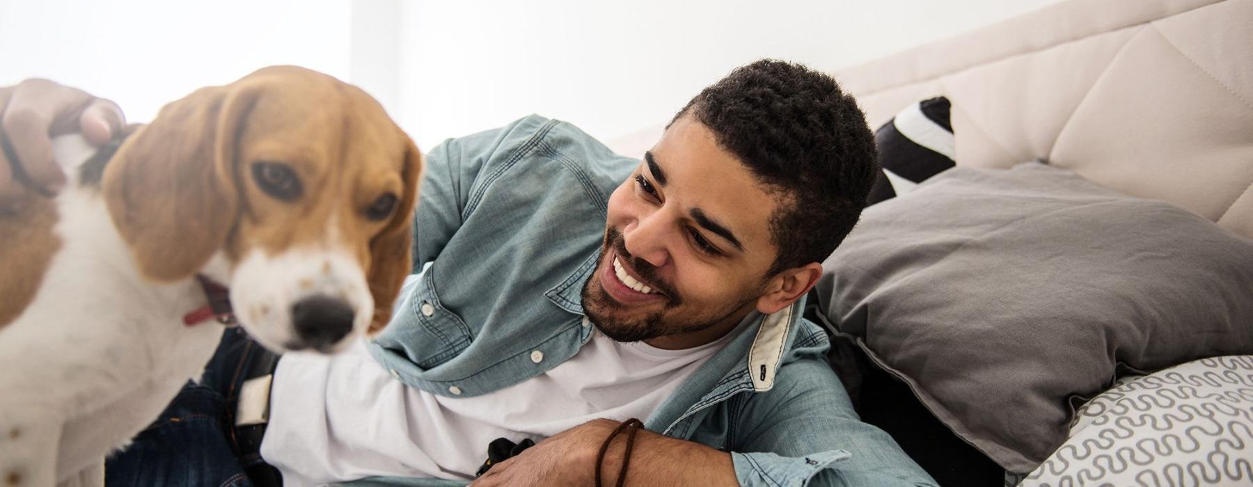 man smiles and pets his dog on a bed
